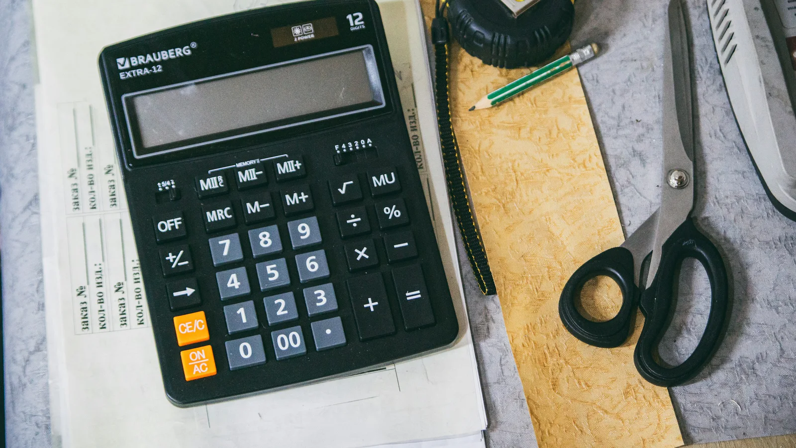 Calculator, pencil, papers, measuring tape, and scissors on a work desk